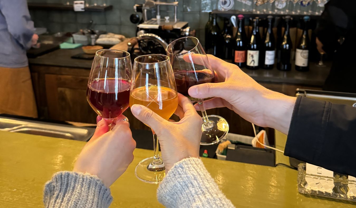 Three hands holding up and clinking wine glasses at a bar in Paris, France