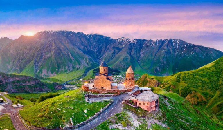 A lone stone church on a small hill in Georgia with towering snow-capped mountains looming in the background