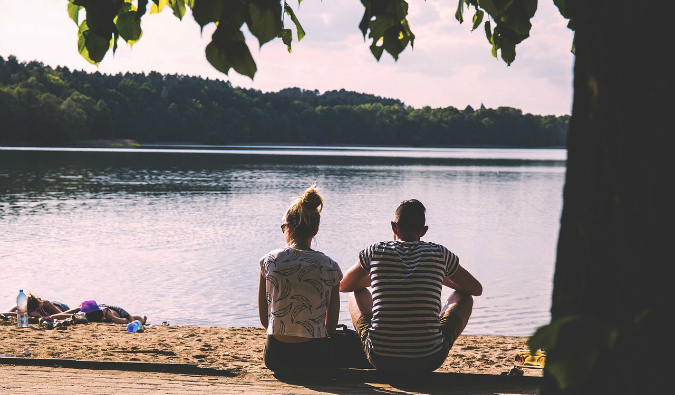 A traveling couple sitting by a large large in the summer