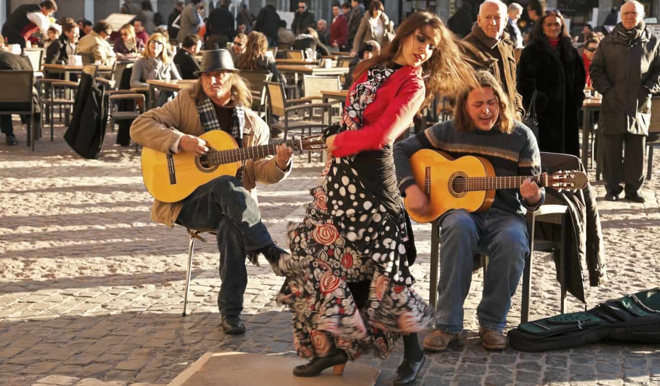 A woman dances flamenco accompanied by two guitar players behind her in a plaza in Madrid, Spain