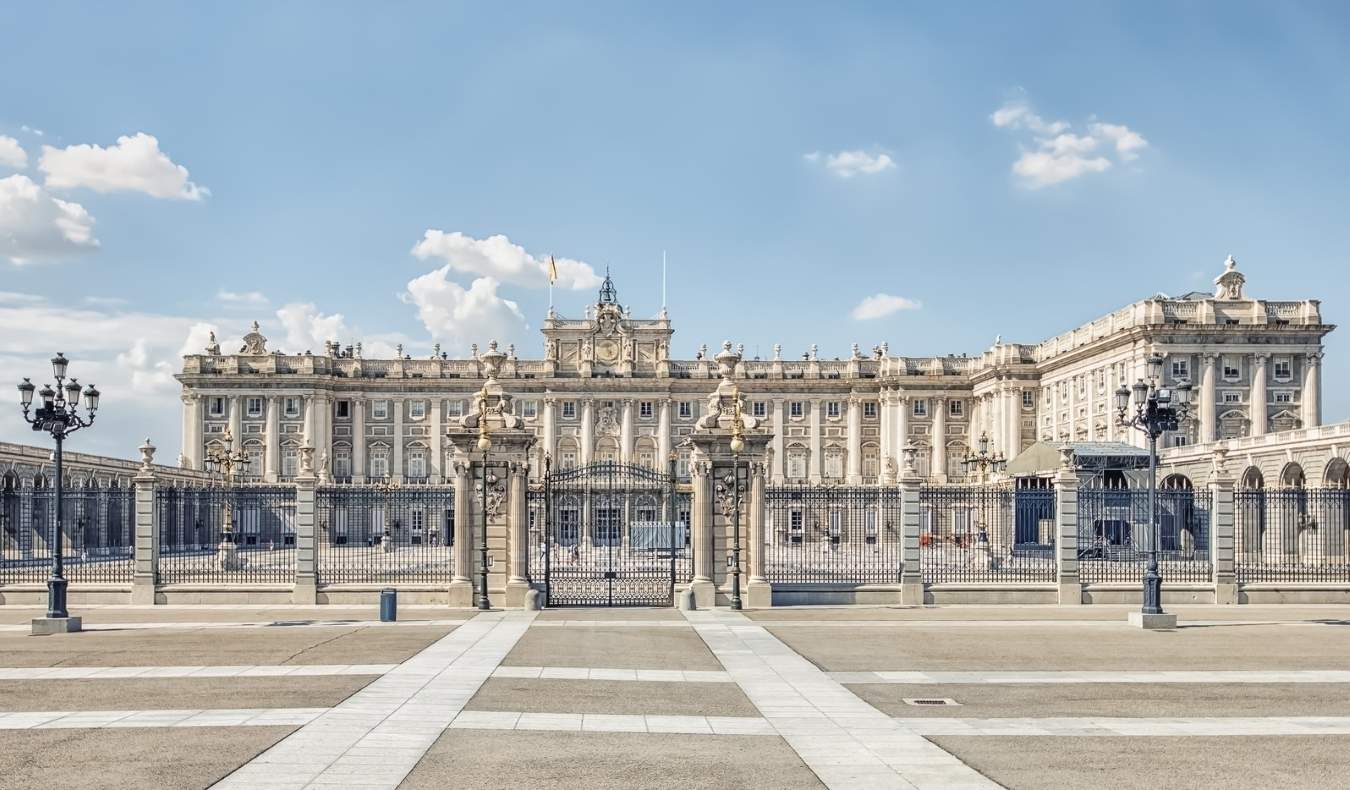 The stone facade of the Royal Palace, with pine trees in front, in Madrid, Spain